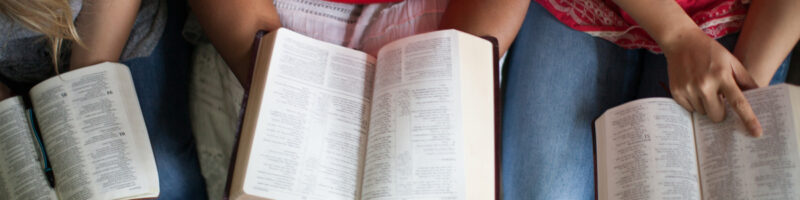 People sitting and reading from open Bibles from an overhead view, engaged in a group Bible study.